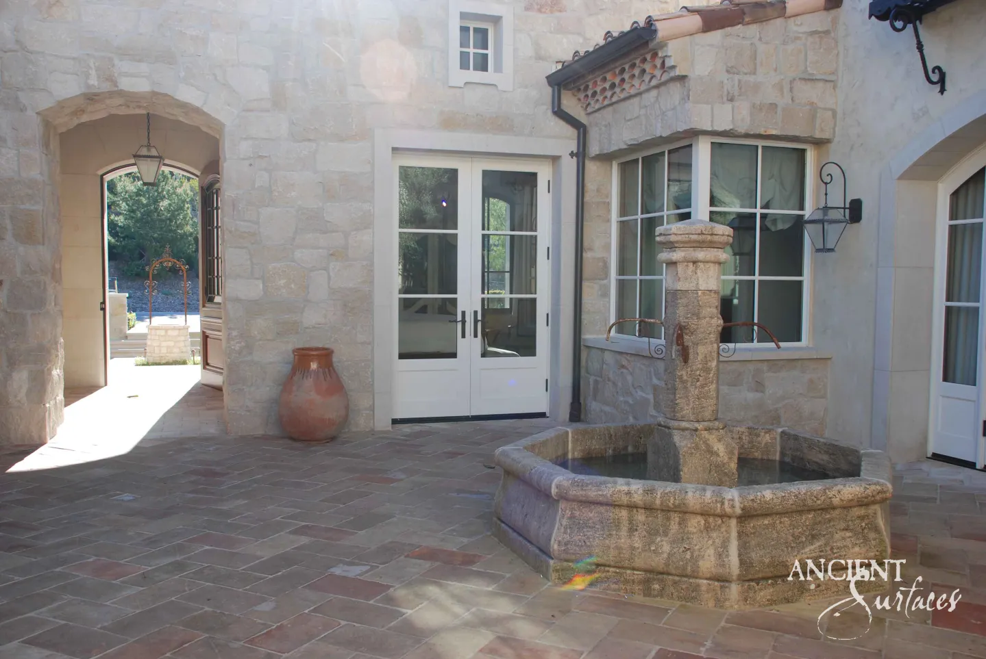 Ancient Surfaces reclaimed octagonal limestone courtyard fountain running on a herringbone terracotta terrace at a stone villa