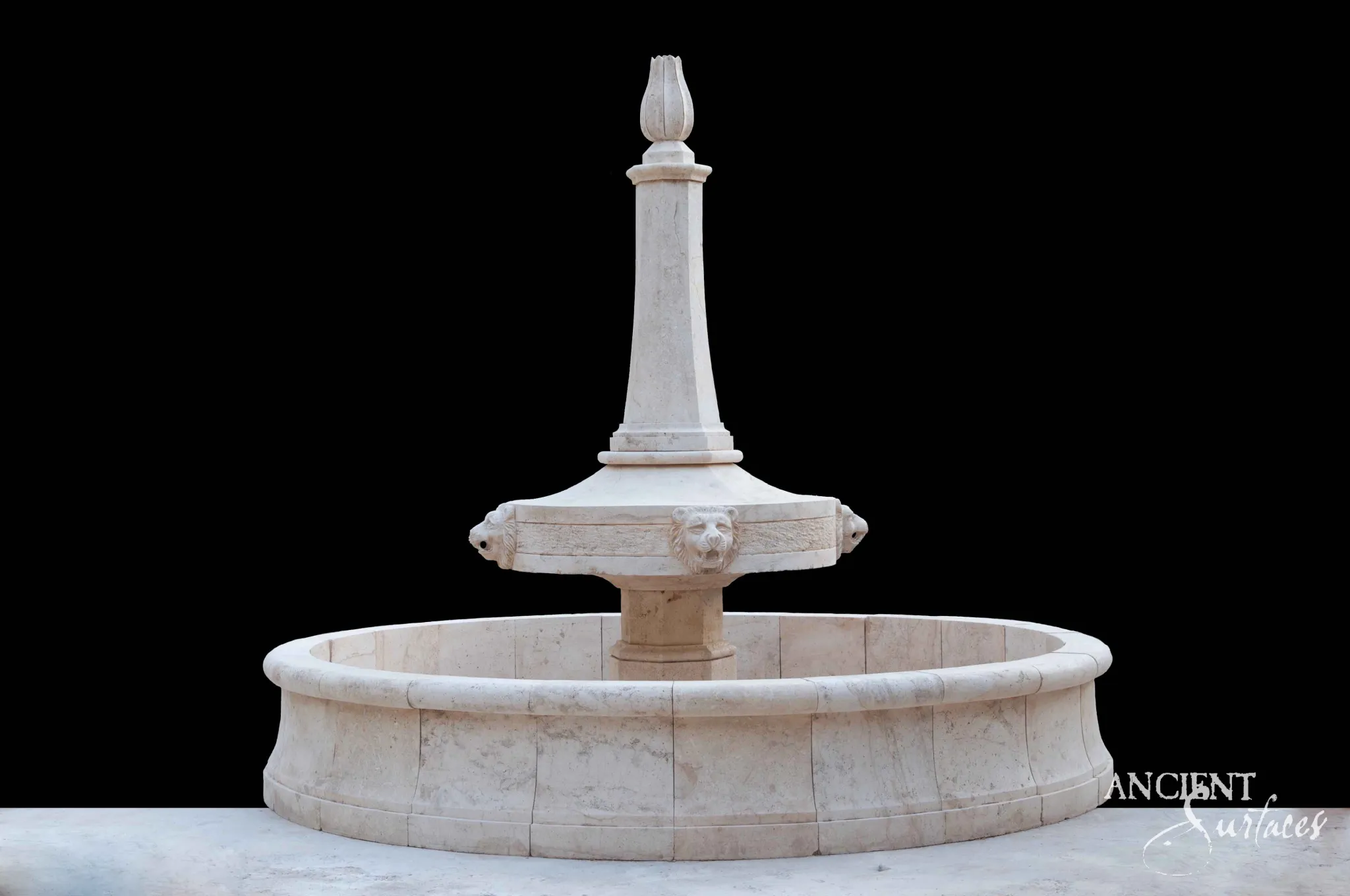 Tall reclaimed limestone fountain from Ancient Surfaces with lion mask spouts on a raised bowl beneath an obelisk shaft and tulip finial