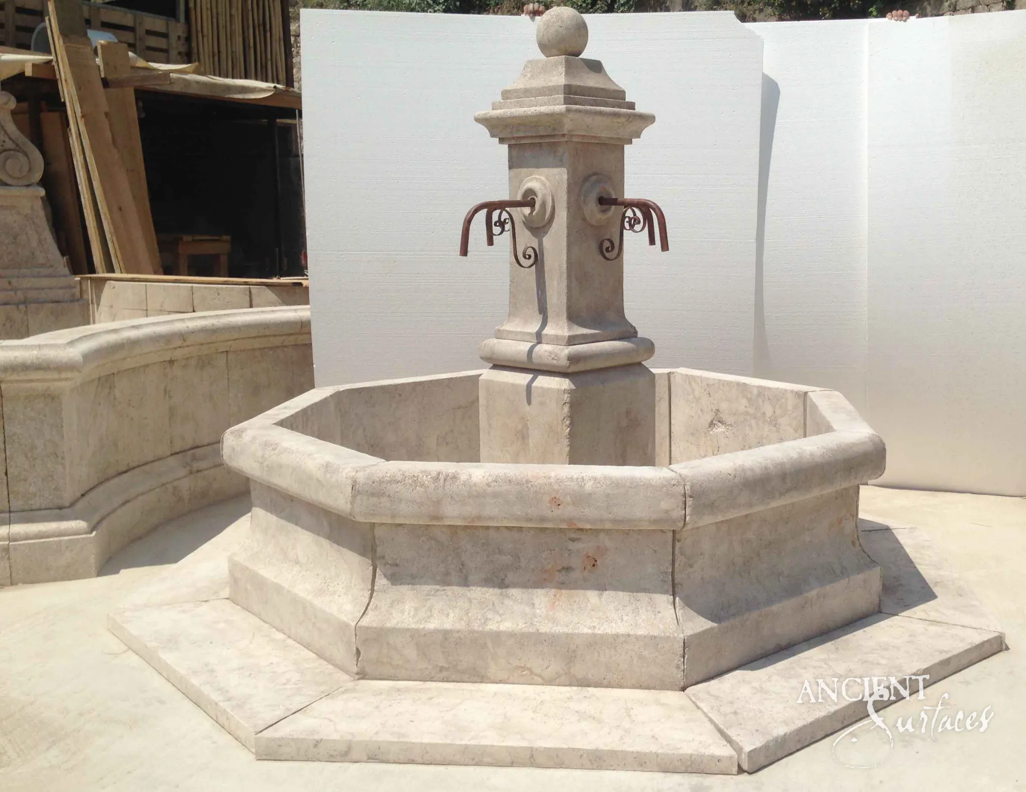 Pale cream reclaimed octagonal limestone fountain from Ancient Surfaces with rosette mounted iron spouts and a stepped stone apron